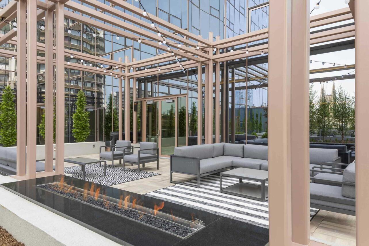 An inviting outdoor terrace featuring modern lounge seating, a sleek linear fire pit, and open pergola design—perfect for gathering and unwinding under the city lights.